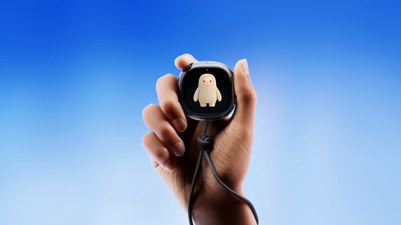 A hand holding Meta Muse Charm with a smiling Muse character visible on the screen against a blue background
